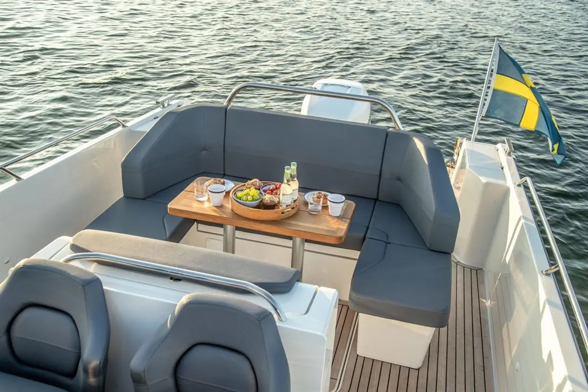 Comfortable boat seating area with a wooden table set with fruit, pastries, and drinks, overlooking serene water.